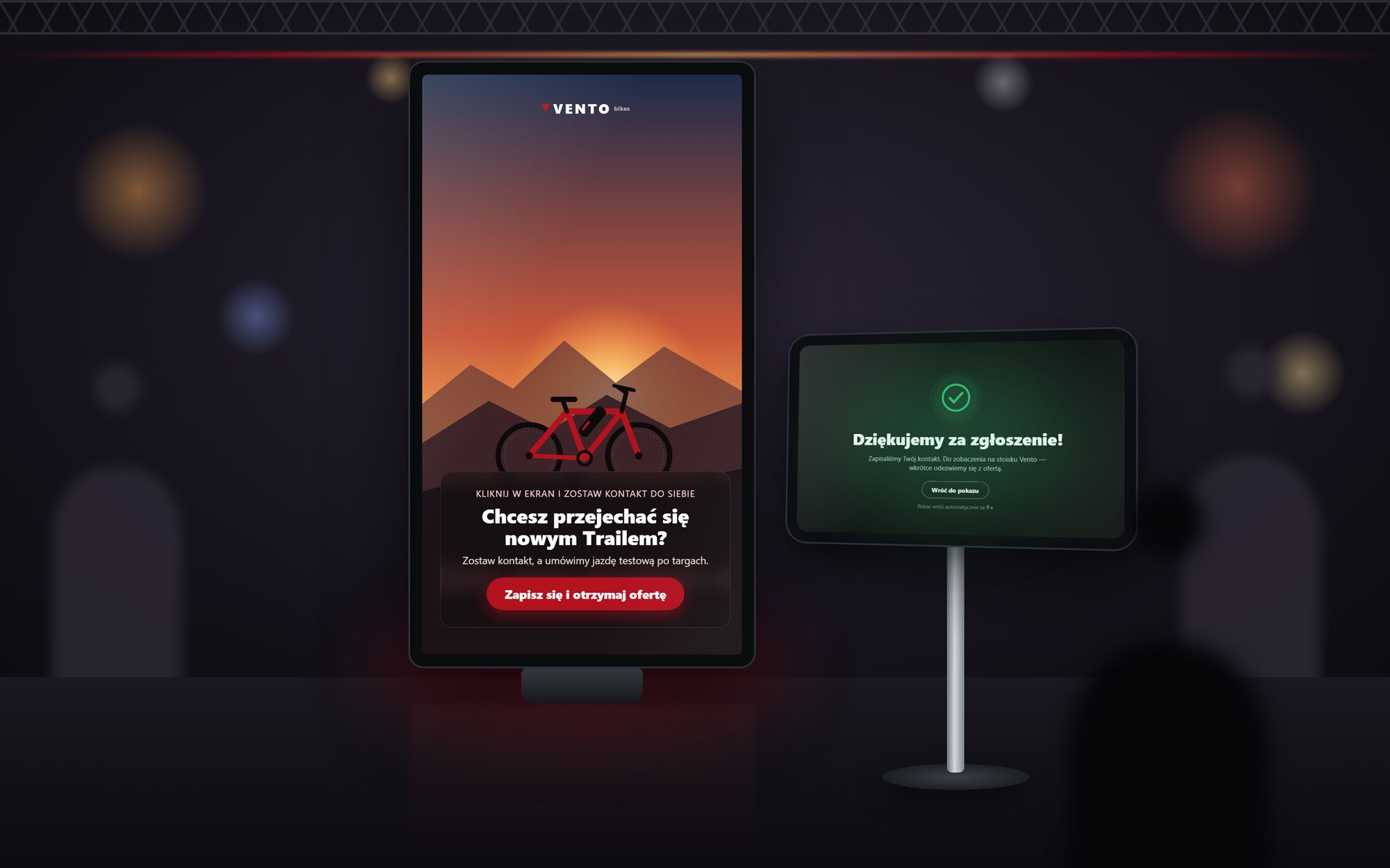 Pionowy monitor na stoisku z filmem i przyciskiem zapisu, obok tablet z podziękowaniem za zgłoszenie